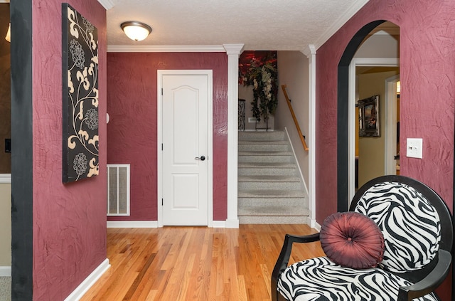 foyer entrance with ornamental molding, decorative columns, light hardwood / wood-style flooring, and a textured ceiling