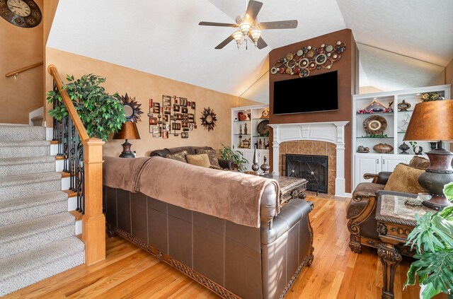 living room with lofted ceiling, light hardwood / wood-style flooring, built in features, ceiling fan, and a fireplace