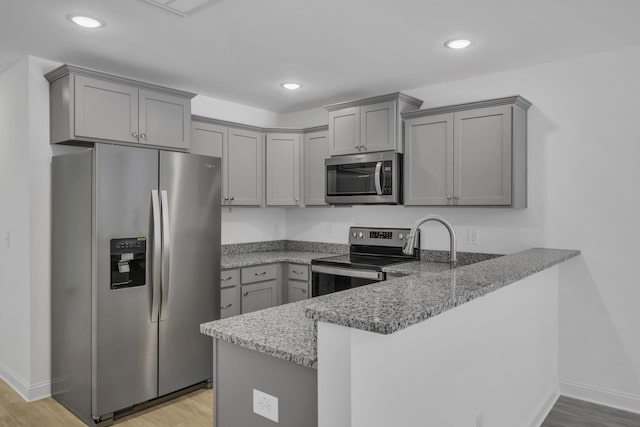 kitchen with appliances with stainless steel finishes, stone countertops, light hardwood / wood-style flooring, and kitchen peninsula