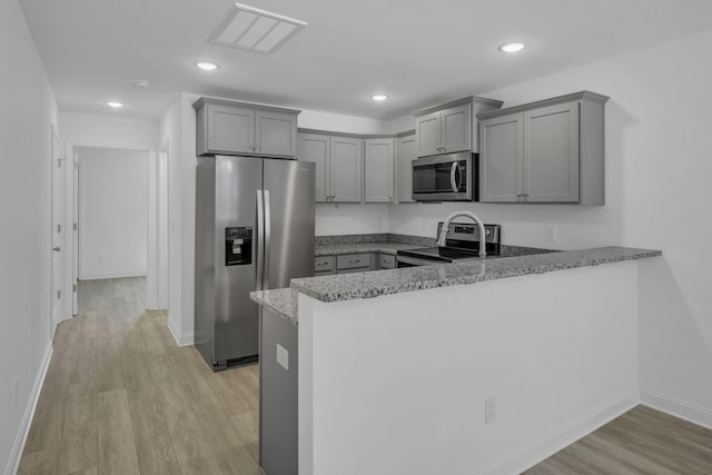 kitchen with stone counters, gray cabinets, appliances with stainless steel finishes, light hardwood / wood-style floors, and kitchen peninsula