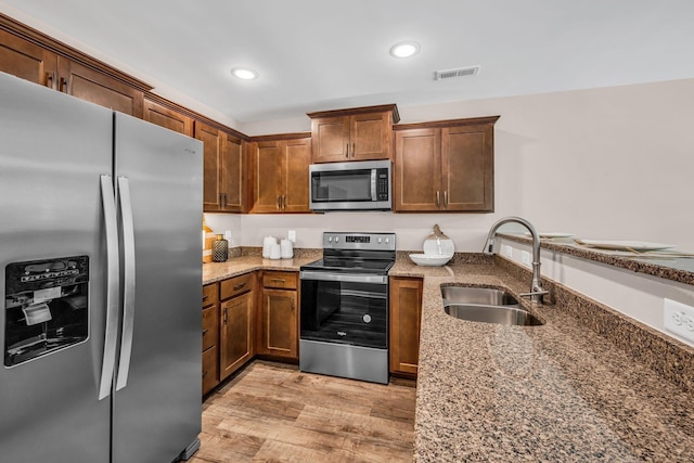 kitchen with appliances with stainless steel finishes, stone countertops, sink, and light wood-type flooring