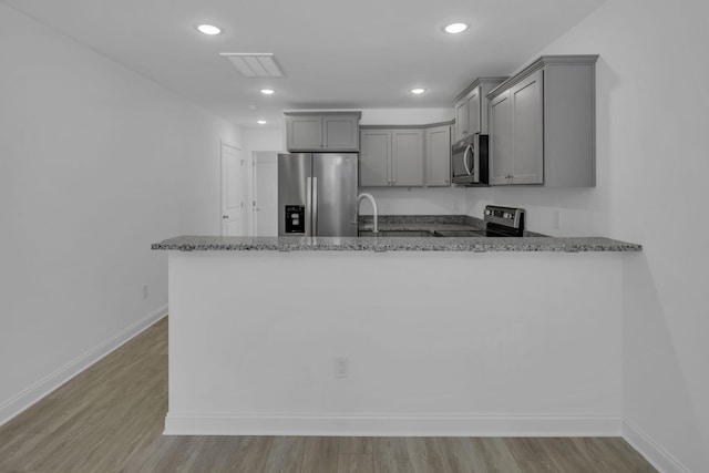 kitchen with gray cabinetry, dark stone countertops, kitchen peninsula, stainless steel appliances, and light hardwood / wood-style flooring