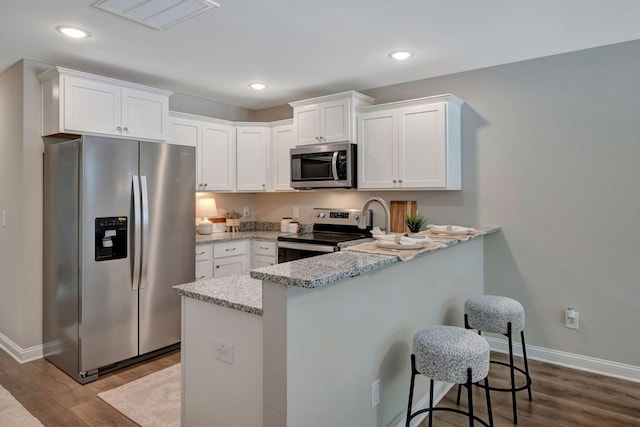 kitchen featuring a breakfast bar, white cabinets, light stone counters, stainless steel appliances, and light hardwood / wood-style flooring