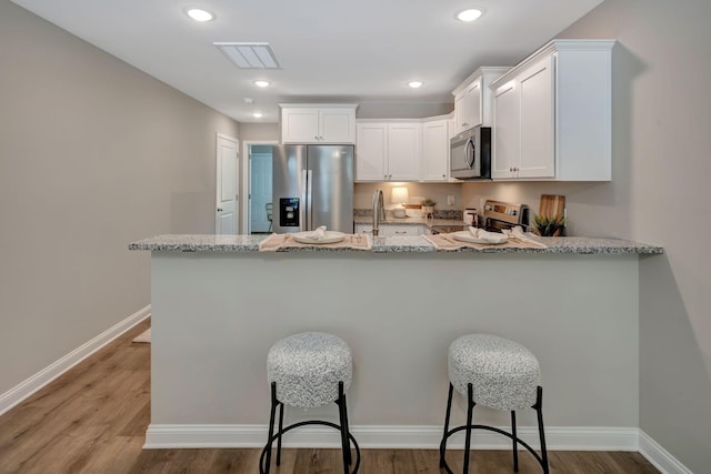 kitchen with light stone countertops, appliances with stainless steel finishes, white cabinets, and kitchen peninsula