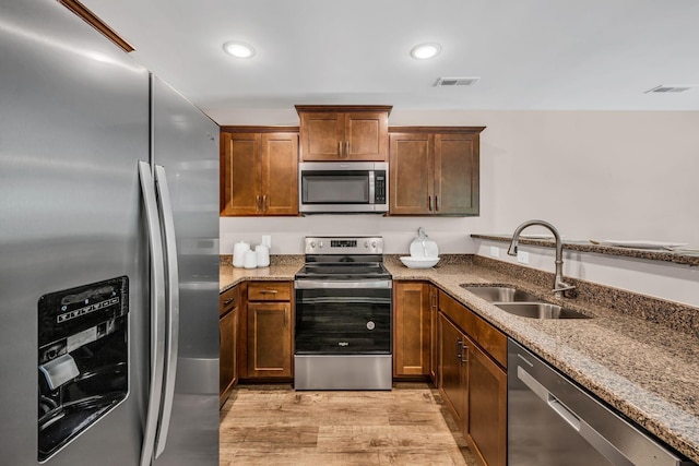 kitchen with stone countertops, sink, light hardwood / wood-style flooring, and appliances with stainless steel finishes