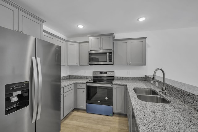 kitchen featuring sink, light stone counters, light hardwood / wood-style flooring, gray cabinets, and stainless steel appliances