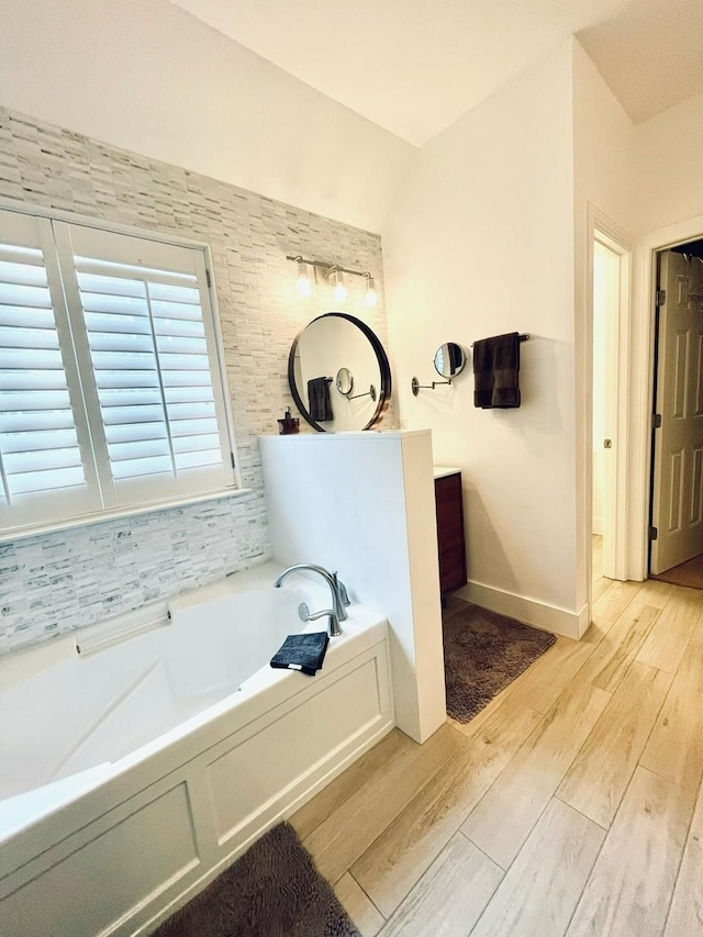 bathroom with hardwood / wood-style flooring, vanity, lofted ceiling, and a bath