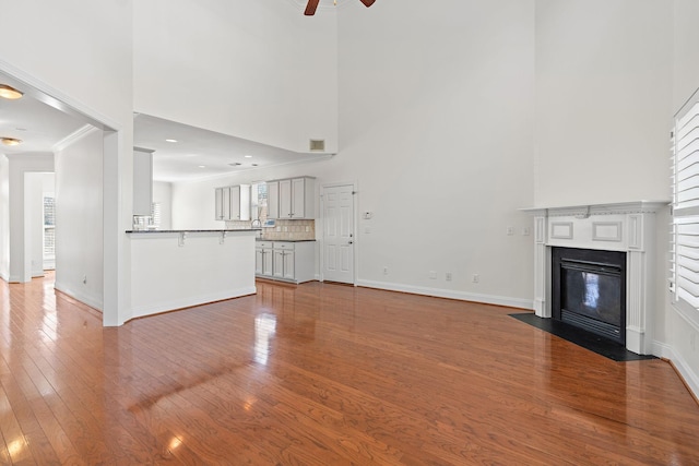 unfurnished living room with hardwood / wood-style flooring, ornamental molding, ceiling fan, and a high ceiling