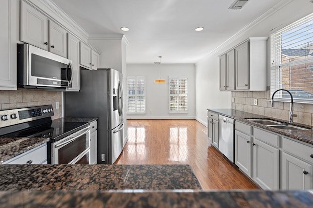 kitchen with sink, crown molding, appliances with stainless steel finishes, pendant lighting, and dark stone counters