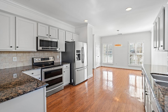 kitchen with stainless steel appliances, crown molding, pendant lighting, and dark stone countertops