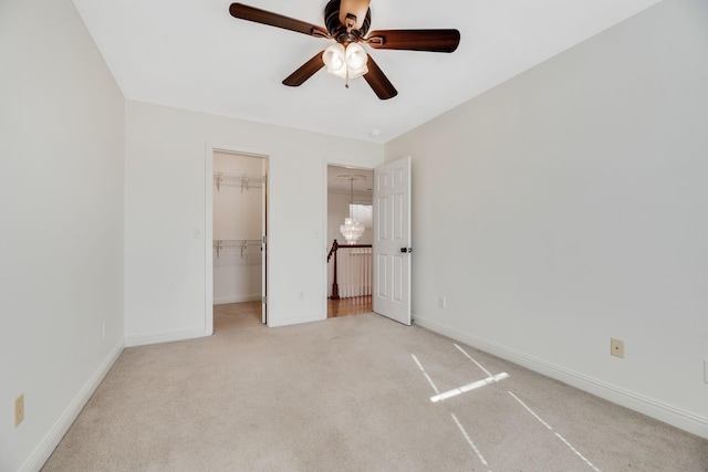 unfurnished bedroom with a walk in closet, light colored carpet, a closet, and ceiling fan