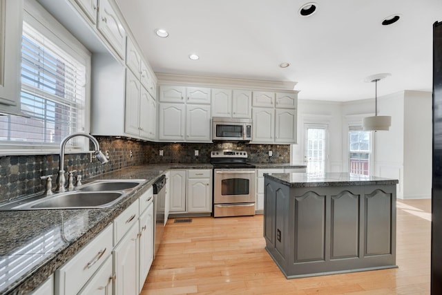 kitchen featuring appliances with stainless steel finishes, white cabinetry, sink, dark stone counters, and hanging light fixtures