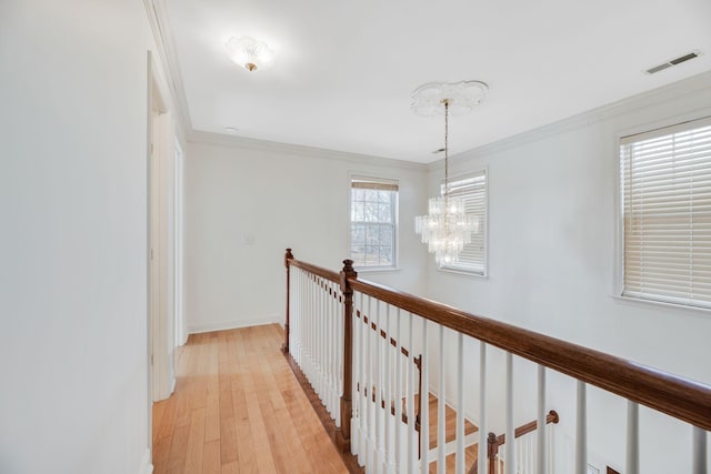 hall with ornamental molding, light wood-type flooring, and an inviting chandelier