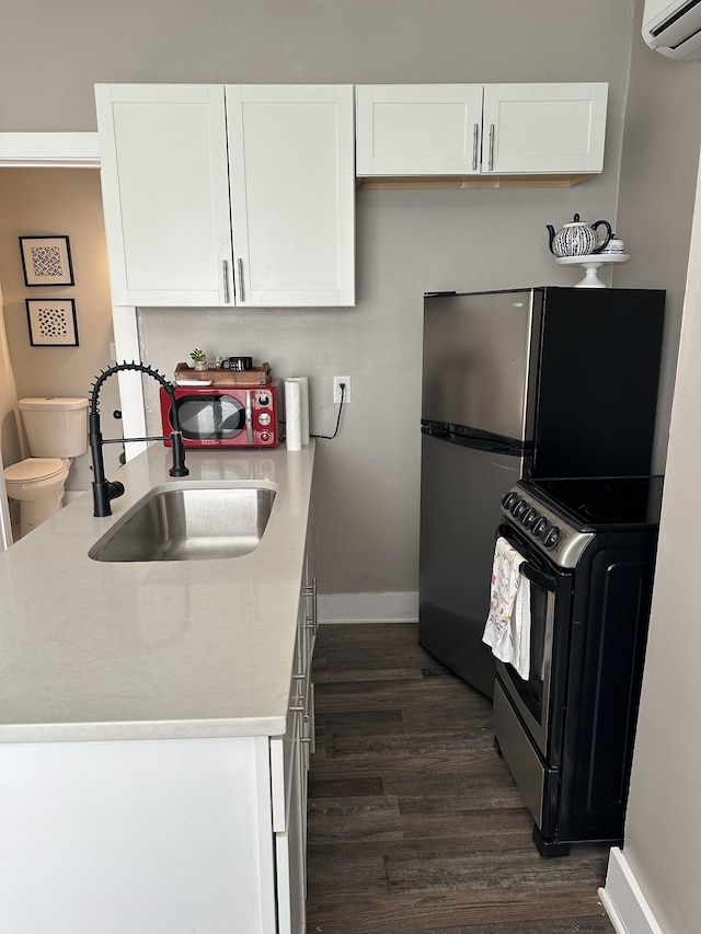 kitchen with sink, stainless steel range with electric stovetop, a wall unit AC, white cabinets, and dark hardwood / wood-style flooring