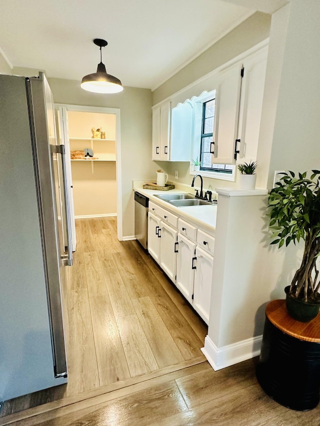 kitchen with sink, white cabinets, hanging light fixtures, stainless steel appliances, and light wood-type flooring