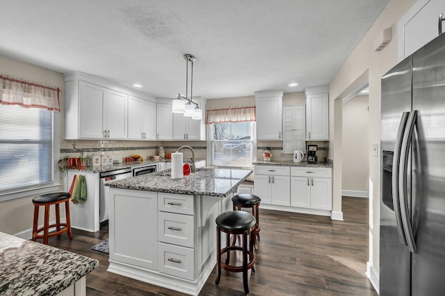 kitchen with hanging light fixtures, appliances with stainless steel finishes, a kitchen island with sink, and white cabinets