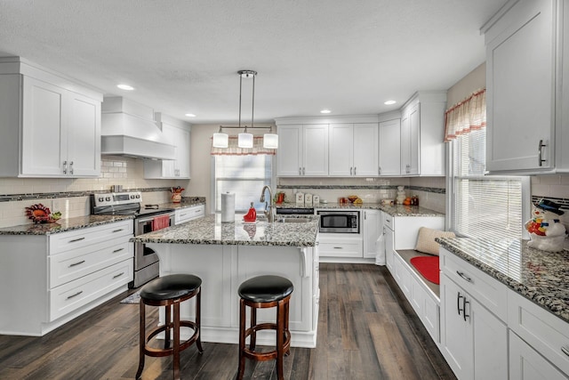 kitchen with custom exhaust hood, an island with sink, white cabinetry, and stainless steel appliances