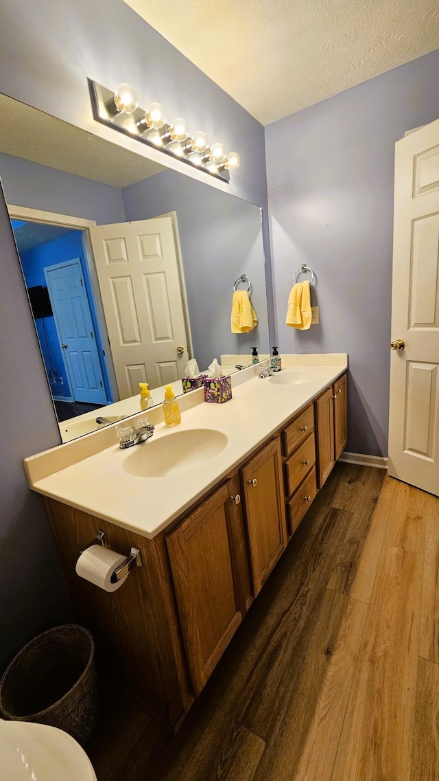 bathroom with a textured ceiling, wood finished floors, a sink, baseboards, and double vanity