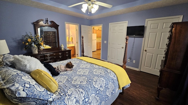 bedroom featuring white refrigerator, ceiling fan, a tray ceiling, and dark hardwood / wood-style flooring