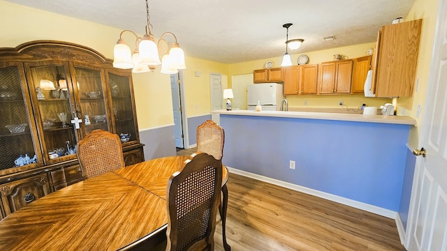 dining area with a textured ceiling, a chandelier, light wood-style flooring, and baseboards