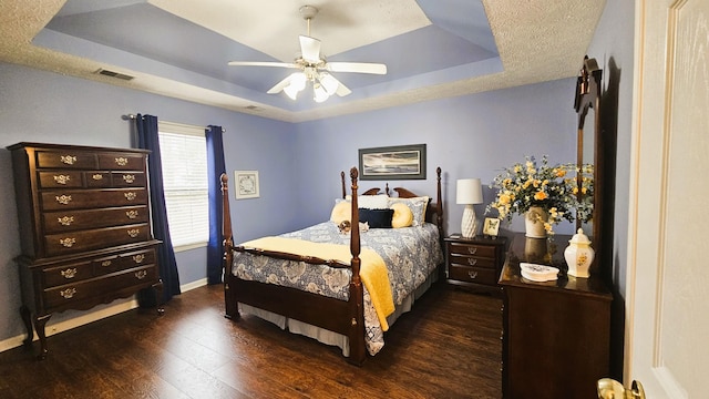 bedroom featuring a raised ceiling, dark wood-type flooring, a textured ceiling, and ceiling fan