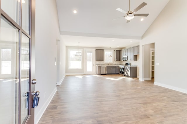 unfurnished living room with sink, light hardwood / wood-style flooring, high vaulted ceiling, and ceiling fan