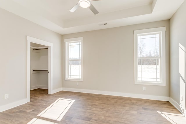 unfurnished bedroom featuring ceiling fan, a walk in closet, a raised ceiling, and light hardwood / wood-style floors