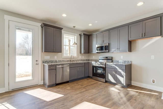 kitchen with pendant lighting, stainless steel appliances, light stone counters, and plenty of natural light