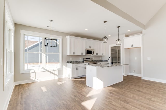 kitchen featuring white cabinetry, stone countertops, hanging light fixtures, appliances with stainless steel finishes, and an island with sink