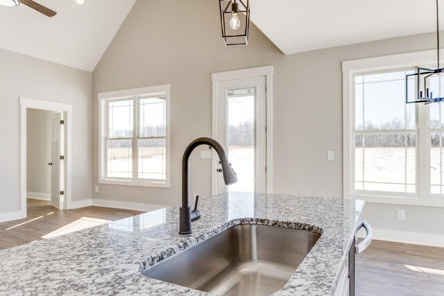 interior details with sink, decorative light fixtures, light hardwood / wood-style flooring, light stone countertops, and ceiling fan with notable chandelier