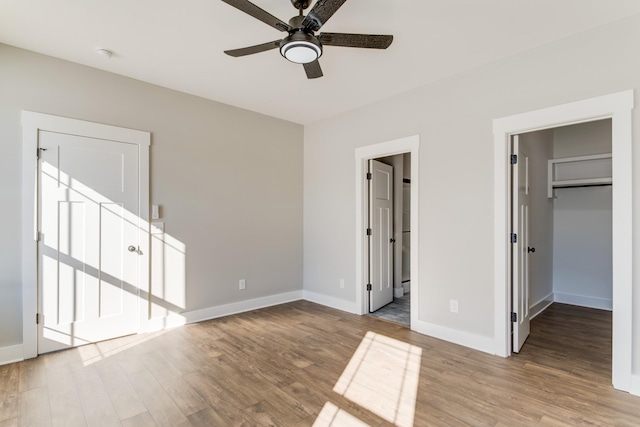 unfurnished bedroom featuring ceiling fan, a spacious closet, light wood-type flooring, and ensuite bath