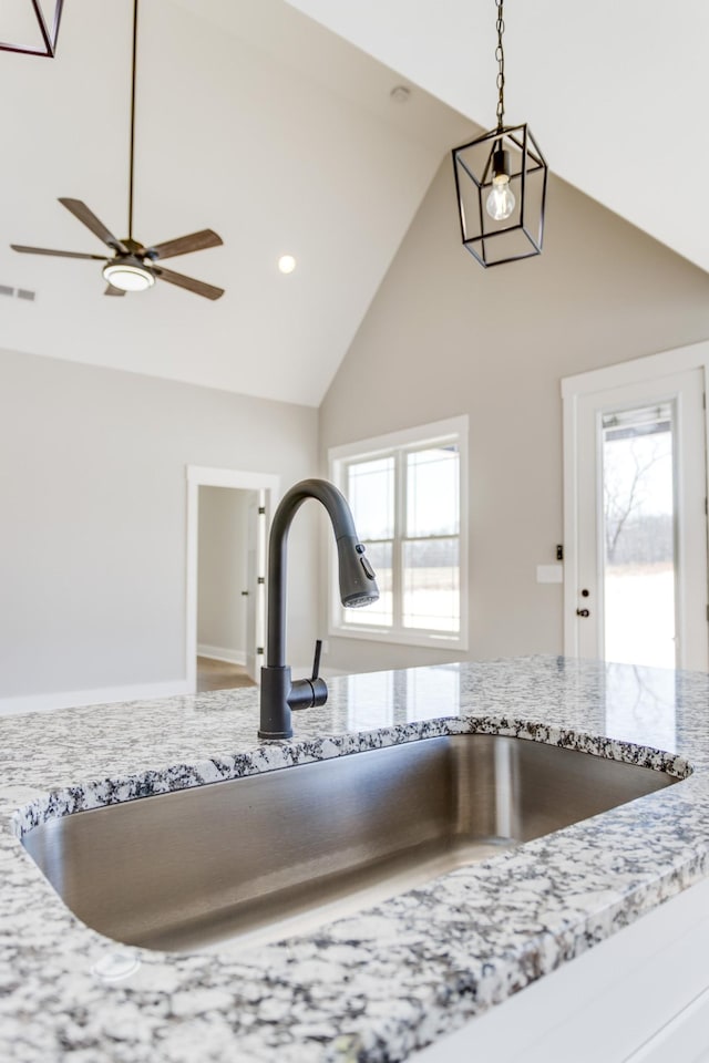 interior details with light stone counters, ceiling fan, decorative light fixtures, and sink