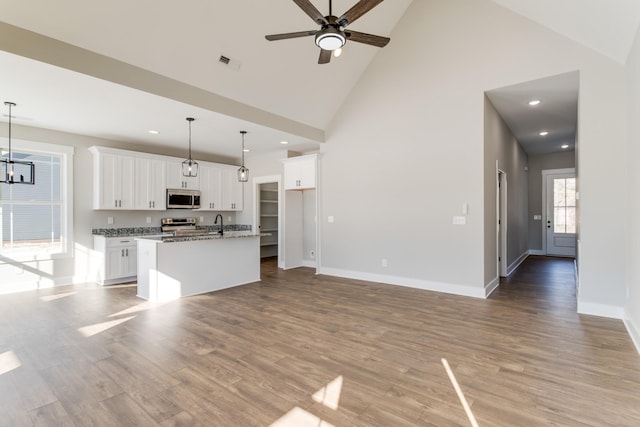 kitchen with decorative light fixtures, appliances with stainless steel finishes, light stone countertops, a kitchen island with sink, and white cabinets