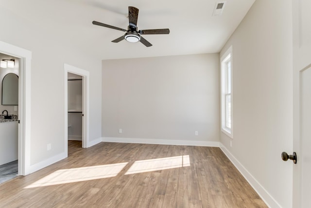 unfurnished bedroom featuring ceiling fan, a walk in closet, a closet, and light hardwood / wood-style flooring