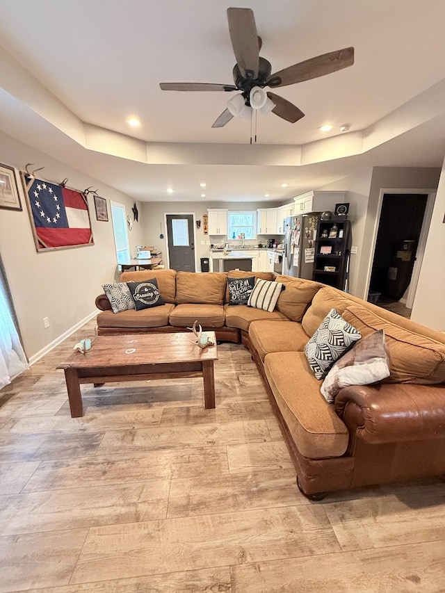 living room featuring plenty of natural light, light hardwood / wood-style floors, a raised ceiling, and ceiling fan