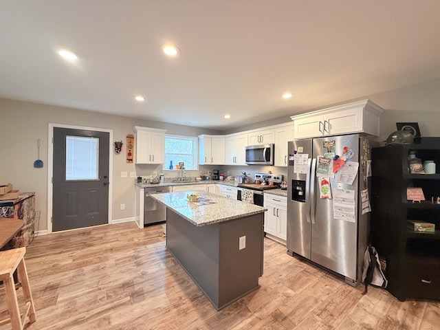 kitchen featuring white cabinetry, stainless steel appliances, a center island, and light stone counters