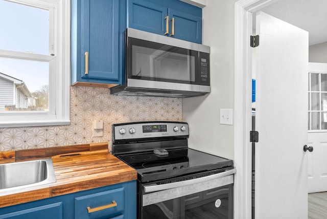 kitchen featuring blue cabinetry, sink, wooden counters, appliances with stainless steel finishes, and backsplash