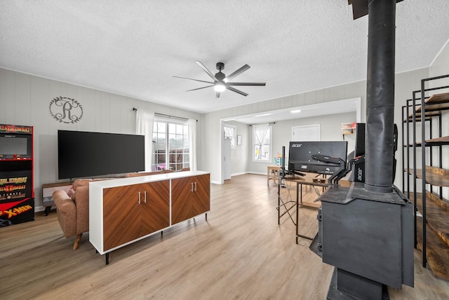 living room featuring ceiling fan, a wood stove, a textured ceiling, and light hardwood / wood-style floors