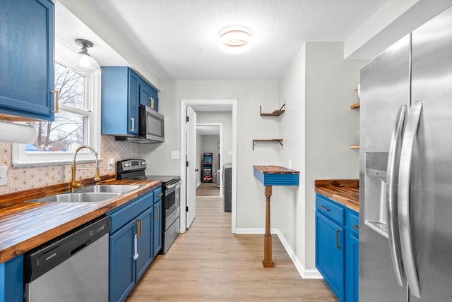 kitchen featuring blue cabinets, appliances with stainless steel finishes, sink, and wood counters