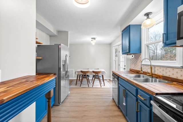 kitchen with blue cabinets, sink, wooden counters, stainless steel appliances, and light hardwood / wood-style flooring