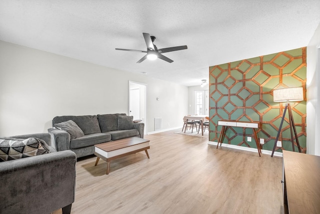 living room featuring ceiling fan, light hardwood / wood-style floors, and a textured ceiling