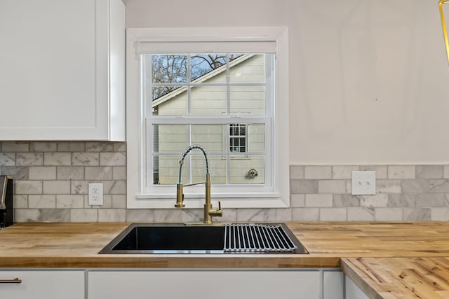 kitchen with white cabinetry, butcher block countertops, decorative backsplash, and sink