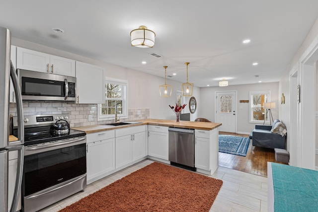 kitchen with appliances with stainless steel finishes, white cabinetry, sink, decorative backsplash, and hanging light fixtures