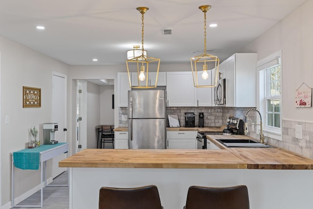 kitchen featuring appliances with stainless steel finishes, white cabinetry, sink, wooden counters, and kitchen peninsula