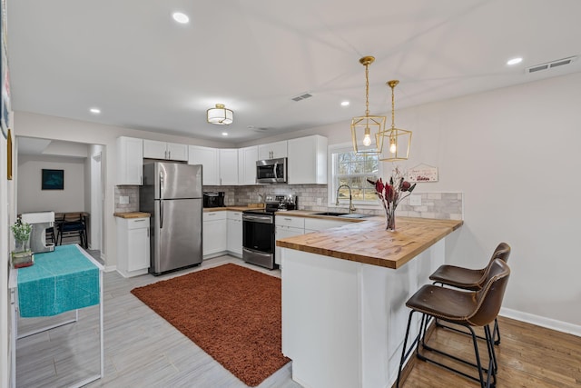 kitchen with a breakfast bar, appliances with stainless steel finishes, white cabinets, wood counters, and kitchen peninsula