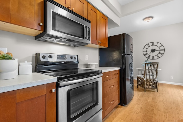 kitchen featuring appliances with stainless steel finishes, light countertops, brown cabinetry, and light wood-style floors