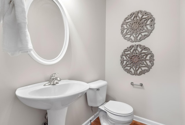 bathroom featuring toilet, baseboards, a sink, and wood finished floors