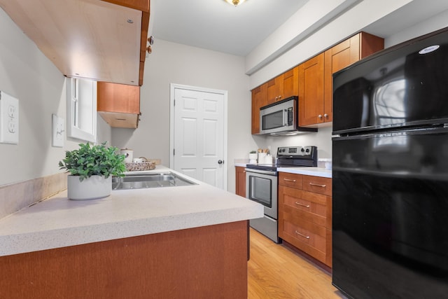 kitchen with light wood-style flooring, appliances with stainless steel finishes, brown cabinets, light countertops, and a sink