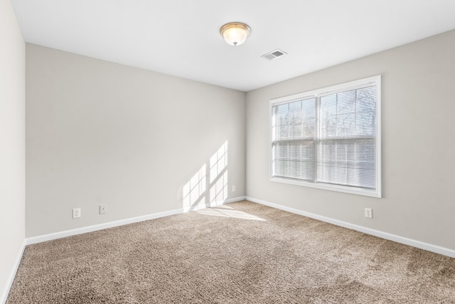 unfurnished room with carpet floors, visible vents, and baseboards