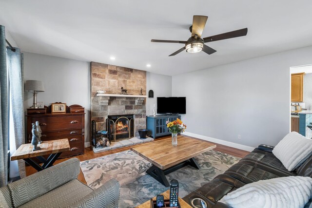 living room featuring a stone fireplace, light hardwood / wood-style floors, and ceiling fan